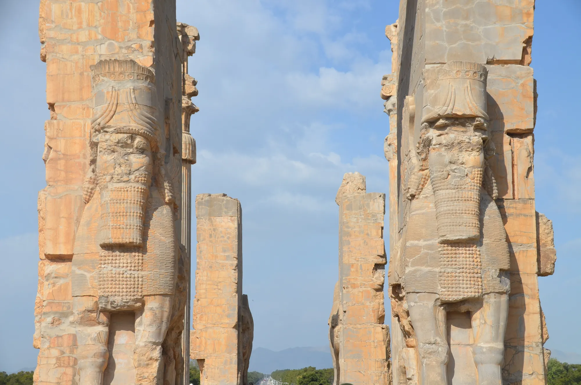 Two stone human-headed winged bulls guard the Gate of All Nations at Persepolis under a blue sky